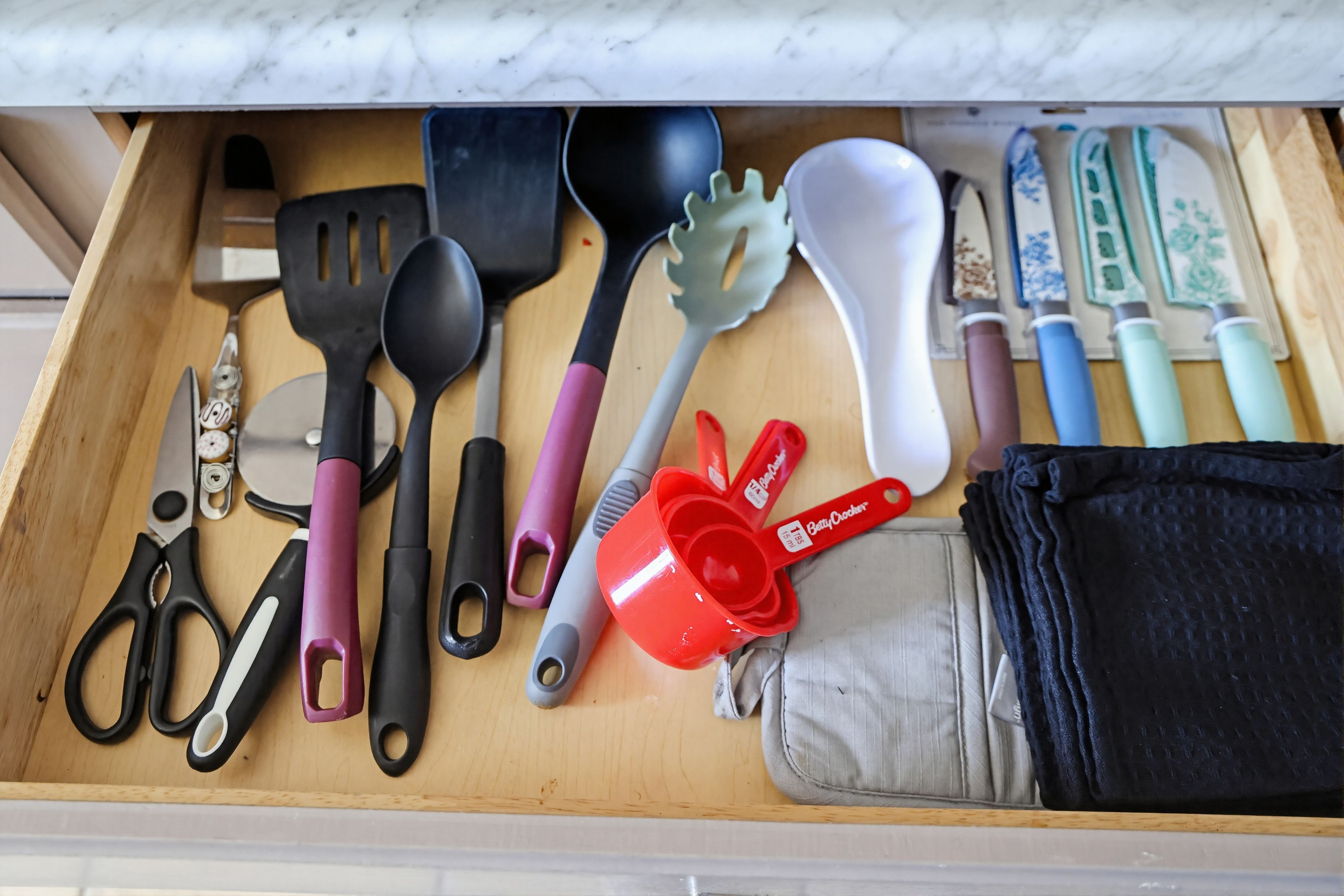A drawer with various kitchen utensils, including spatulas, a whisk, and measuring cups.