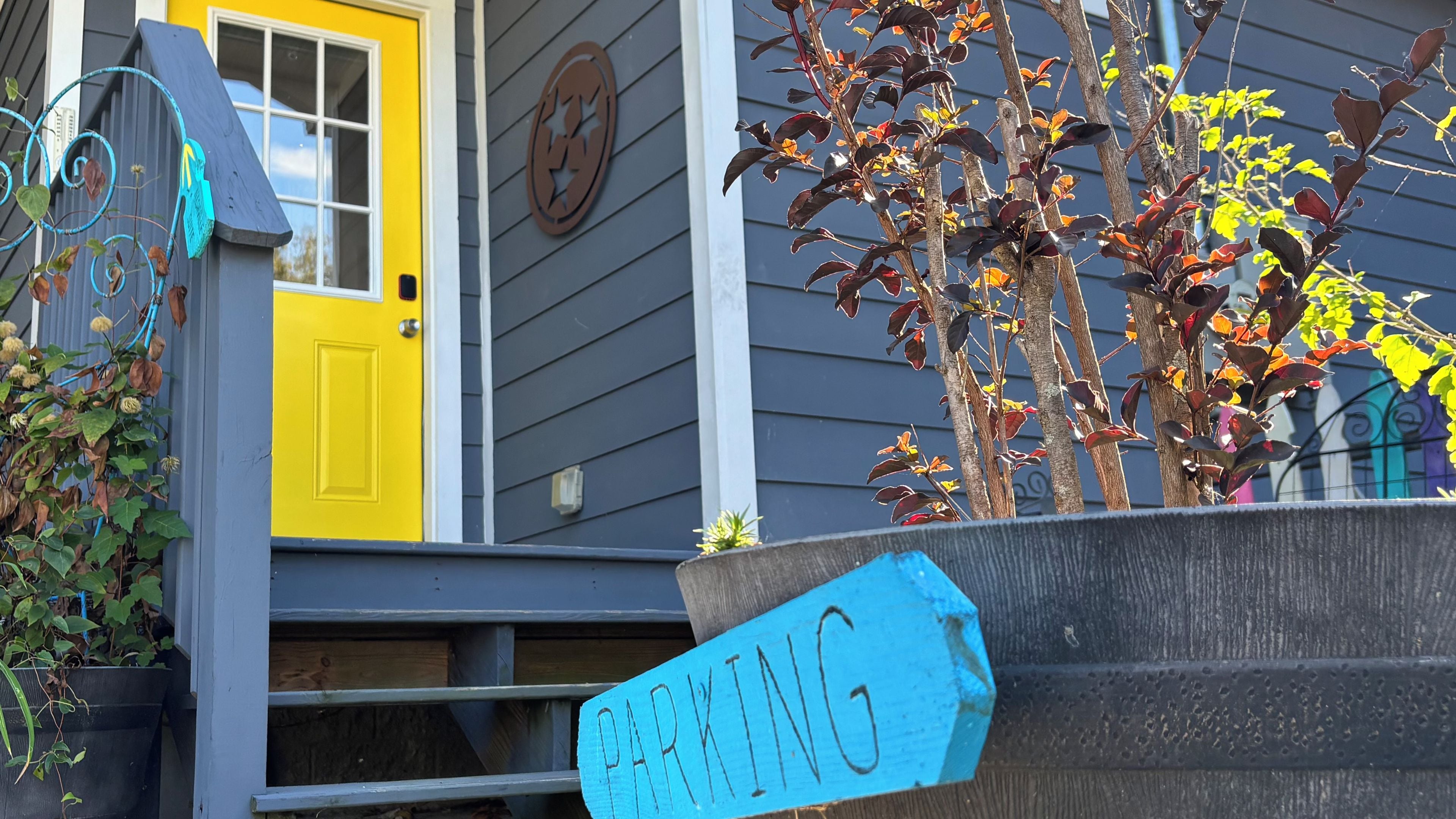 A house with a yellow door, a blue sign indicating parking, and a tree with autumn leaves.