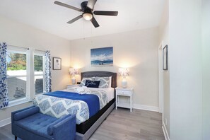 A bedroom with a bed, a chair, a ceiling fan, a nightstand, a lamp, a painting, and a window with curtains. - Heated Pool 3BR home Ybor, close to everything! (Tampa)