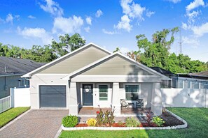 Uma casa residencial com garagem, varanda frontal e jardim ajardinado.