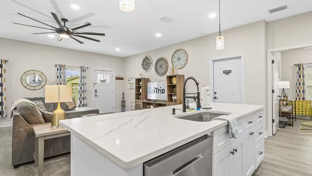 Una cocina moderna con una isla central, un ventilador de techo, luces colgantes y un comedor con sofá y lámpara.