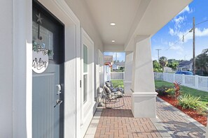 A covered porch with a welcome sign, outdoor seating, and a view of the neighborhood. - Heated Pool 3BR home Ybor, close to everything! (Tampa)