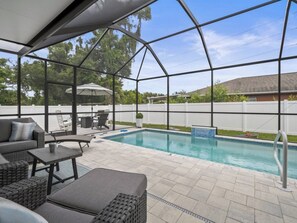 Ett takförsett utomhusområde med en pool, sittplatser och utsikt över trädgården.
