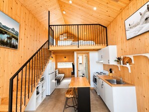 Eine kompakte, moderne Holzhütte mit Schlafzimmer im oberen Bereich, Küchenzeile und Essbereich.