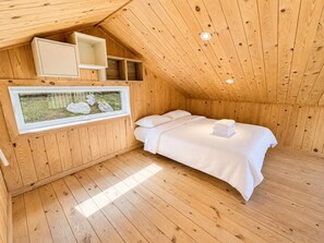 Una habitación de madera con una cama, un ventanal con vistas a rocas y una estantería con un espejo.