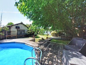 Ein Schwimmbecken mit Holzterrasse, einem Basketballkorb und einem Haus im Hintergrund.