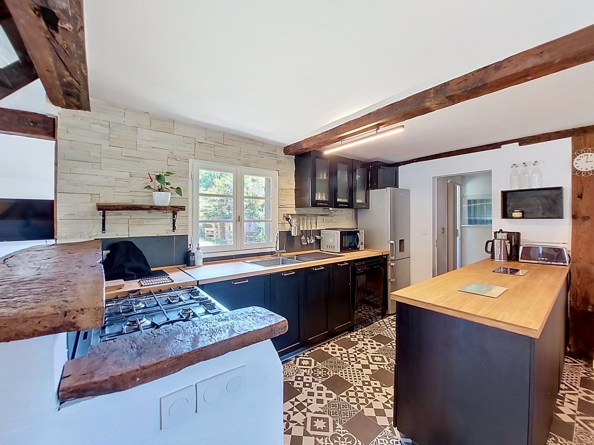 A kitchen with a gas stove, dark cabinets, a wooden countertop, and patterned floor tiles.