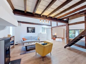 A spacious living area with a high ceiling, wooden beams, a sofa, a yellow chair, and a coffee table. - La landaise by Interhome (Saint-Vincent-de-Tyrosse)