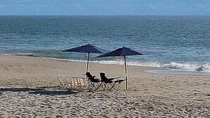 Ein Strand mit zwei Sonnenschirmen, einem Stuhl und einem kleinen Tisch.