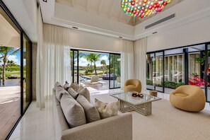 Ein modernes Wohnzimmer mit einer Couch, Sesseln, einem Couchtisch und großen Fenstern mit Blick ins Freie.