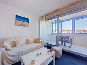 A modern living room with a sofa, a coffee table, and a balcony with a view of buildings. - Le point d'Or by Interhome (Hossegor)