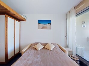 Ein Schlafzimmer mit einem Bett, einem Strandbild, einem Fenster mit Vorhängen und einem Thermostat an der Wand.