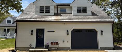 Une maison à deux étages avec une porte d’entrée sombre, un garage et un petit porche agrémenté de plantes en pot.