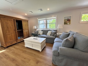 A living room with a wooden cabinet, a grey sofa, a white coffee table, and a window with blinds.