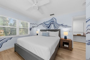 A bedroom with a bed, two bedside tables with lamps, a ceiling fan, and a window with blinds.