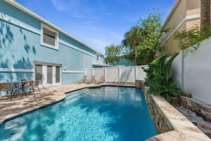 A swimming pool with a stone border, a white fence, and a table with chairs.