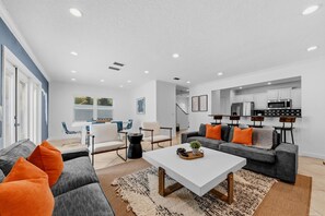Una sala de estar moderna con un sofá, sillones, una mesita de centro y una cocina al fondo.