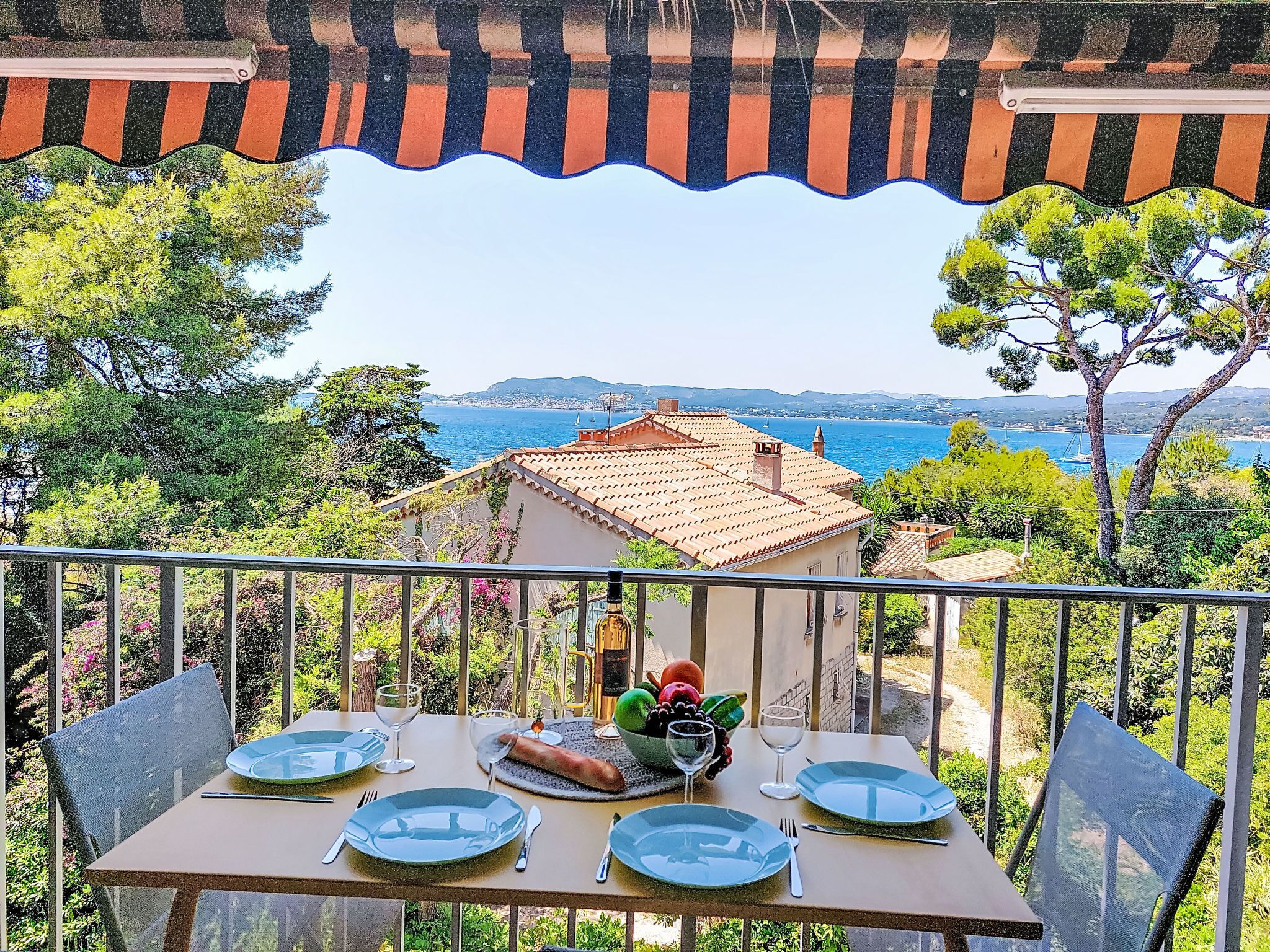 A balcony with a table set for two, overlooking a coastal view with buildings and trees.