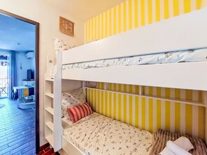 Een stapelbed met streepjesbeddengoed, een klein bureau met een stoel en een televisie.
