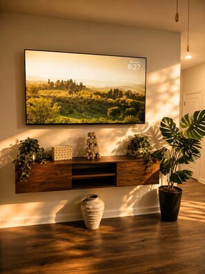 A modern living room with a mounted TV displaying a landscape, a wooden console table with decorative items, and a potted plant. - Modern Lakeview Oasis, King Bed • Gym • Pool (Jacksonville)