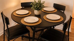 Una mesa redonda para comer con cuatro sillas, una planta en maceta y platos con manteles individuales.