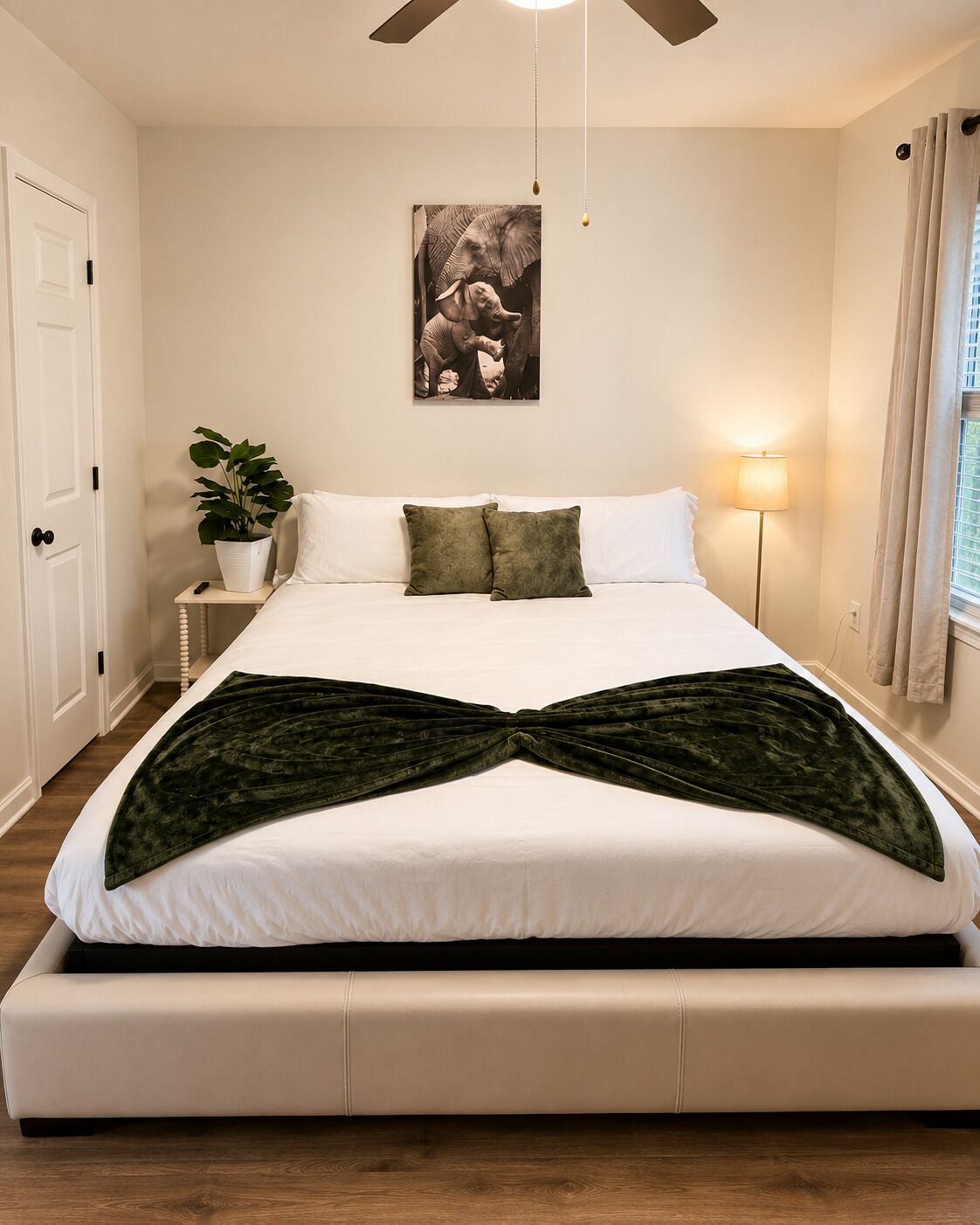 A bedroom with a bed, a potted plant, a wall-mounted picture, and a floor lamp.