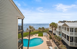 A pool with a view of the ocean, a covered deck area, and a building with multiple balconies. - 731 North Hampton - New to Program - Stunning Ocean Views (Fripp Island)