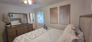 Ein Schlafzimmer mit Bett, Schminktisch, Spiegel und zwei an der Wand befestigten Kunstwerken.