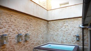 A stone-walled room with a rectangular bathtub, stone flooring, and three wall-mounted lanterns. - Ideal for a group of 4 families, between two natural parks, the sea and Port Aventura. (Camarles)