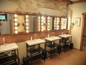 Casa de banho com várias lavatórios, espelhos com iluminação e chão em mosaico.