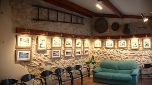 A room with a stone wall, wooden beams, a teal sofa, and framed pictures. - Ideal for a group of 4 families, between two natural parks, the sea and Port Aventura. (Camarles)