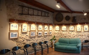 Een kamer met een stenen muur, houten balken, een blauwgroene bank en ingelijste foto's.