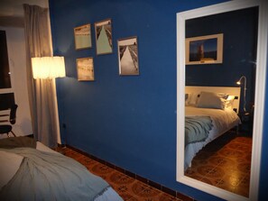 Quarto com cama, mesa de cabeceira, luminária, espelho e parede com quadros.