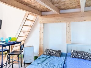 Ein Schlafzimmer mit Dachstockzimmer-Optik, einem Bett mit gemusterten Kissen, einem Tisch mit Stühlen und einer Heizung.