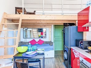 Une pièce compacte avec un lit en mezzanine, un coin repas avec une table et des chaises, un lave-linge et une porte verte.