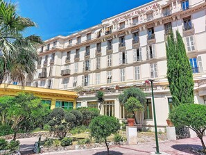 Een hotel met meerdere verdiepingen, балконы, een verzorgde tuin en een helderblauwe lucht.