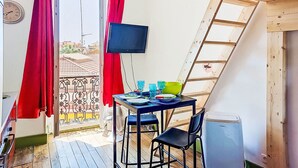 Quarto com teto de madeira, televisão fixada na parede, mesa com cadeiras e janela com cortinas vermelhas.