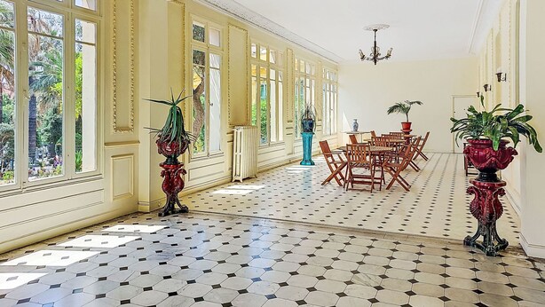 Um quarto espaçoso com janelas amplas, piso estampado e área de jantar com cadeiras e mesas de madeira.