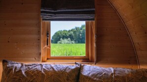 Una habitación con ventana, paredes de madera y una cama con almohadones estampados.