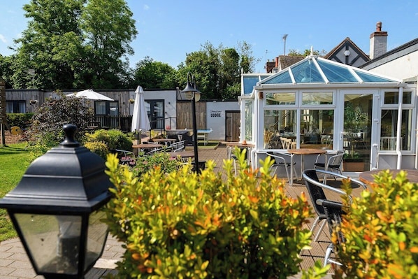 A garden patio area with outdoor seating, a glass-roofed structure, and a sign for 'Serratone Lodge.'