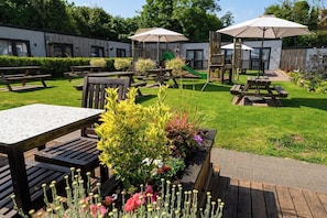 A patio area with picnic tables, a wooden deck, and a small garden with various plants. - Shepherd's Hut Lodge (Shenstone)