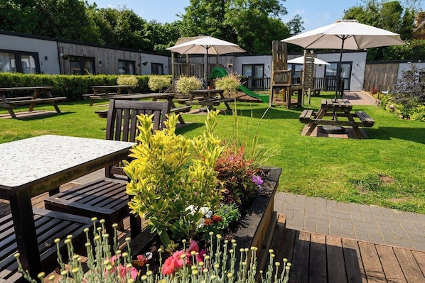 A patio area with picnic tables, a wooden deck, and a small garden with various plants.