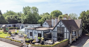 A traditional pub with outdoor seating, a garden area, and a sign indicating it serves food and drinks. - Shepherd's Hut Lodge (Shenstone)
