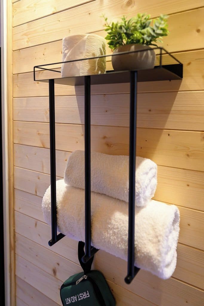 A wooden wall with a metal towel rack holding two folded towels and a potted plant.