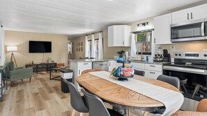 Une cuisine moderne avec des meubles blancs, un four à micro-ondes et une cuisinière. On y trouve également un coin repas avec une table et des chaises en bois.
