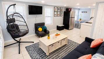 Een moderne woonkamer met een hangstoel, een bank, een salontafel en een keukenhoek met een koelkast en een wastafel.