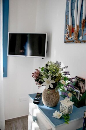 Ett rum med en tv som är monterad på väggen, en vas med blommor på en byrå och en fjärrkontroll.