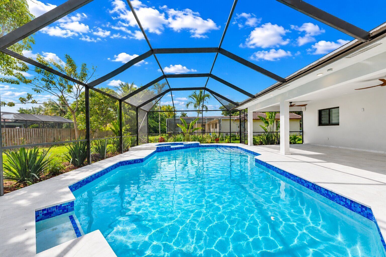 A swimming pool with a glass ceiling, surrounded by a white wall and greenery.