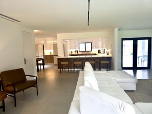 A modern living room with a white sofa, a wooden chair, and a kitchen area with a bar. - Coral Springs Oasis Retreat (Coral Springs)