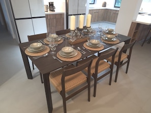 A dining table set with plates, glasses, and cutlery, surrounded by woven chairs. - Coral Springs Oasis Retreat (Coral Springs)